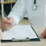 Ein Arzt bespricht mit einer Patientin oder einem Patienten medizinische Unterlagen an einem Schreibtisch.