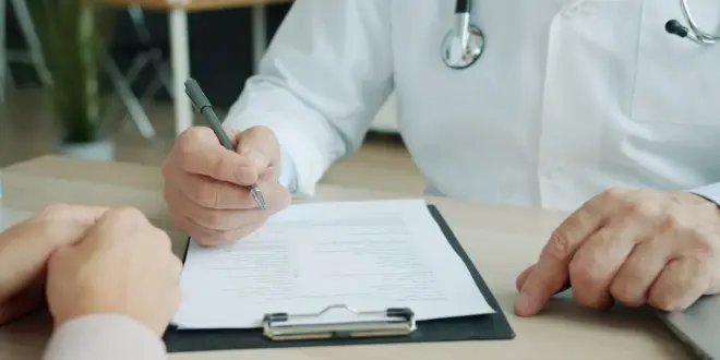 Ein Arzt bespricht mit einer Patientin oder einem Patienten medizinische Unterlagen an einem Schreibtisch.
