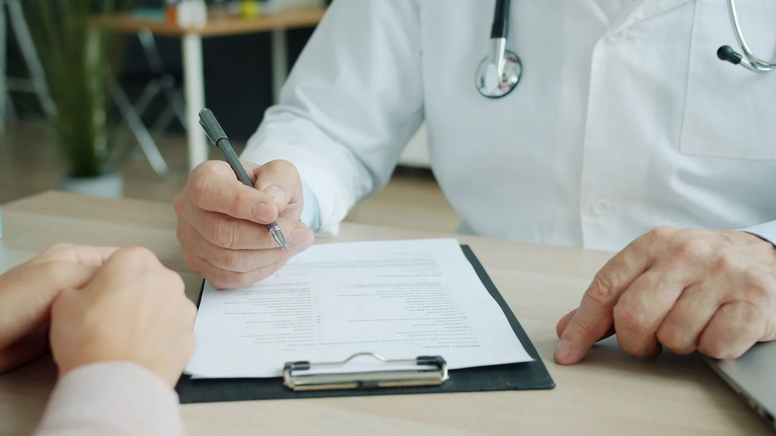 Ein Arzt bespricht mit einer Patientin oder einem Patienten medizinische Unterlagen an einem Schreibtisch.