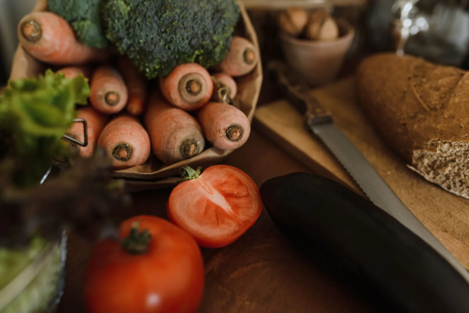Karotten, Brokkoli, Tomaten, Avocado und Vollkornbrot liegen auf einem Holztisch.