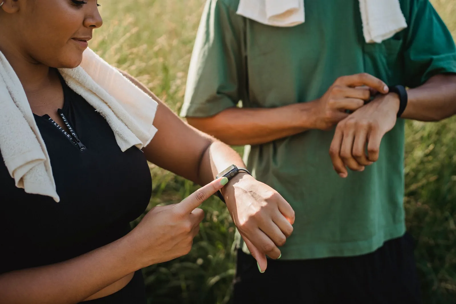 Zwei Personen mit Handtüchern um die Schultern bedienen ihre Sportuhren im Freien.